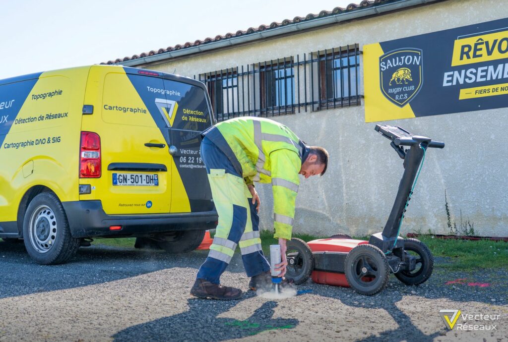 Roadworker in high-visibility gear kneels on asphalt, using a tool beside a yellow survey van labelled Topographie and Détention de Réseaux2.0%